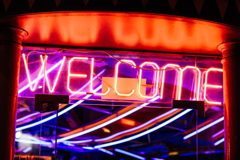 Neon lights spelling welcome against a mirrored background.