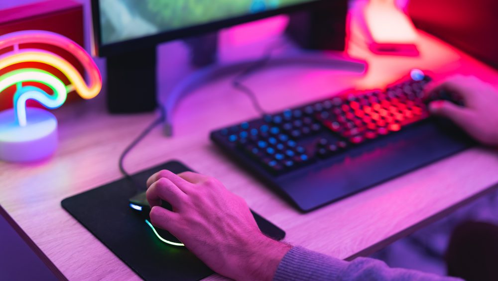 Hands on mouse and keyboard lit by neon lights.