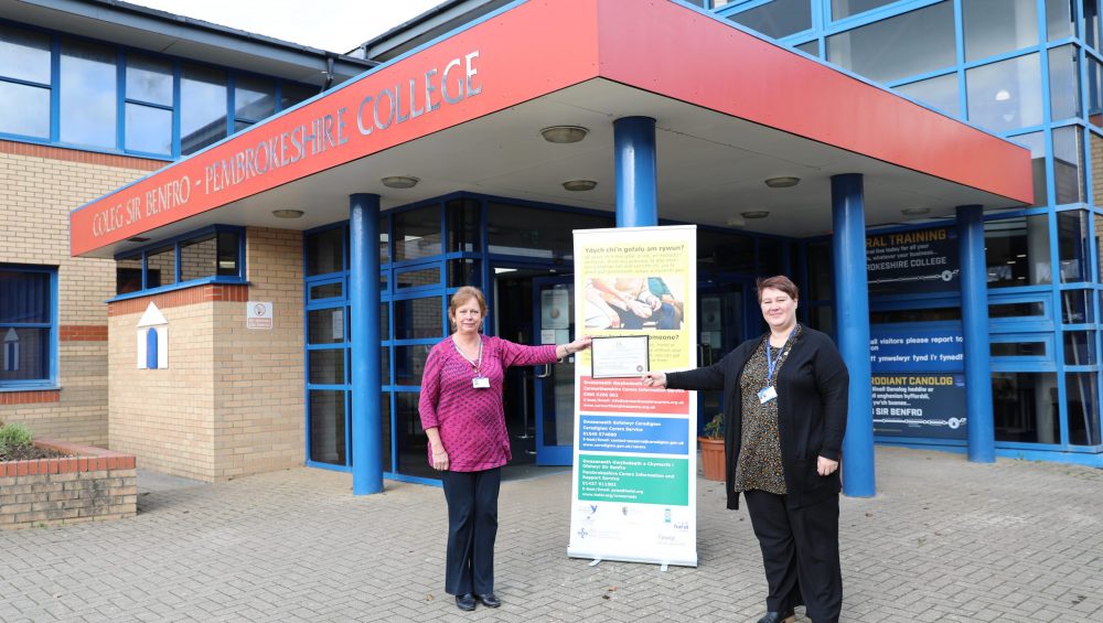 Two members of staff holding certificate outside College entrance.