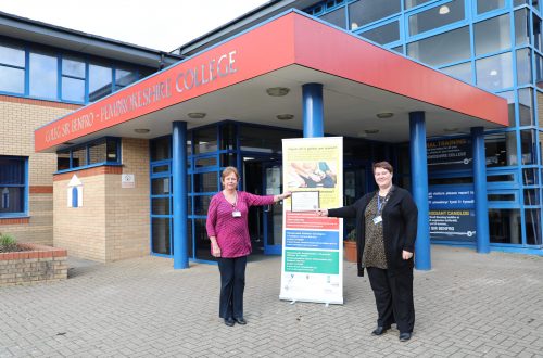 Two members of staff holding certificate outside College entrance.