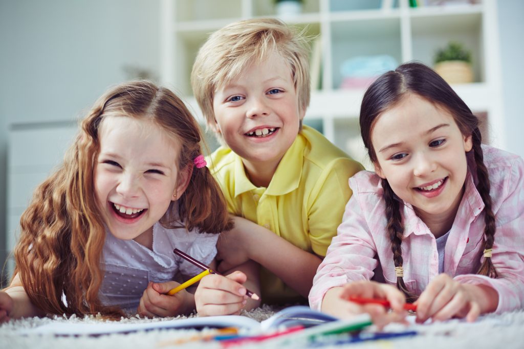 Three smiling children drawing.