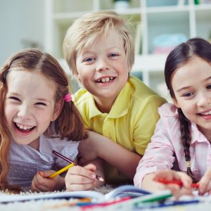 Three smiling children drawing.