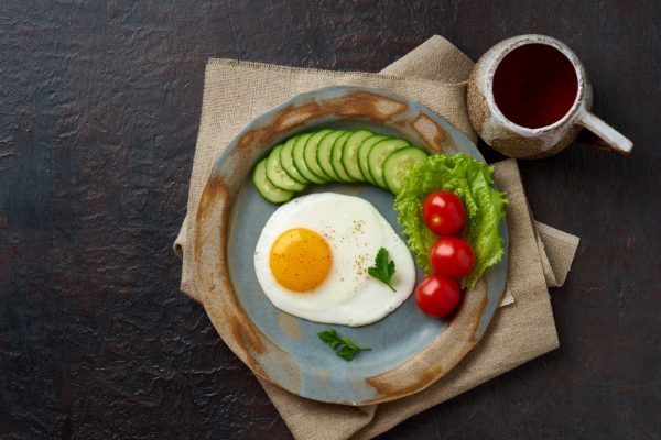 Food on plate, fried egg, slices of cucumber, tomato and lettuce.