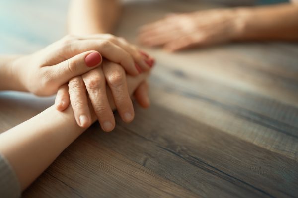 Close up image of younger hands holding older hand.
