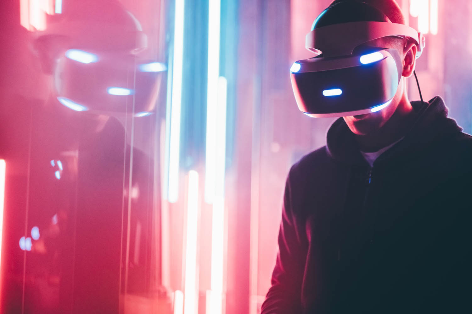 Person yn gwisgo clustffon VR wrth ymyl goleuadau neon