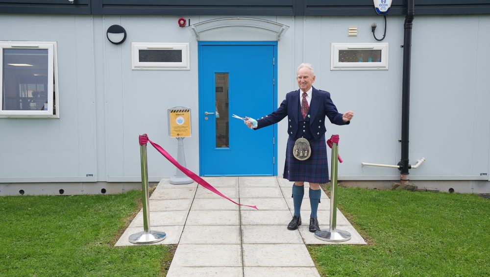 John Burns cutting ribbon outside Centre for Learning building.