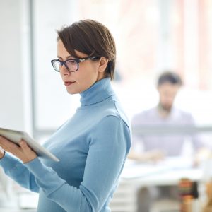 Woman checking digital tablet standing by filing cabinets.