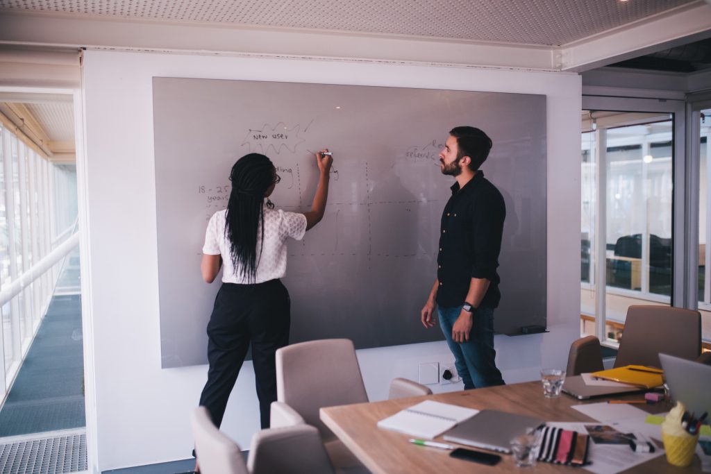 Two people writing project plan on board in office.