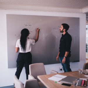 Two people writing project plan on board in office.