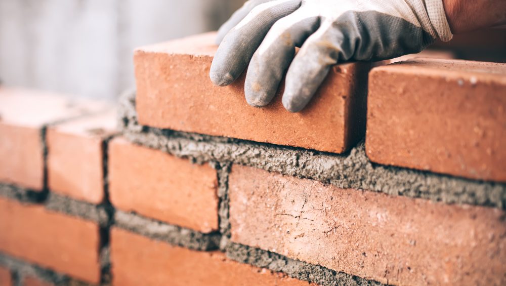 Close up of gloved hand laying brick on wet cement.