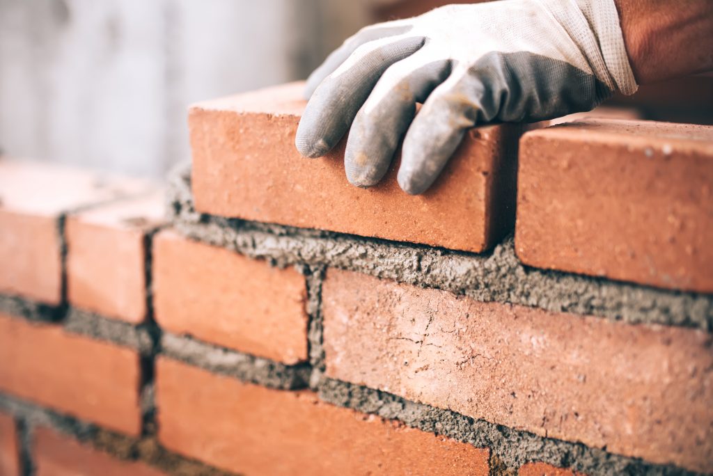 Close up of gloved hand laying brick on wet cement.