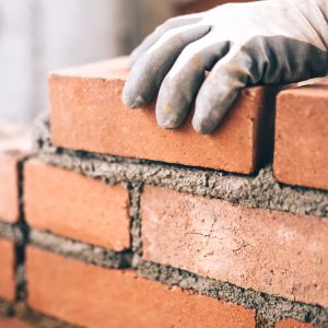 Close up of gloved hand laying brick on wet cement.