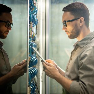 Man looking at digital tablet in front of network server rack.