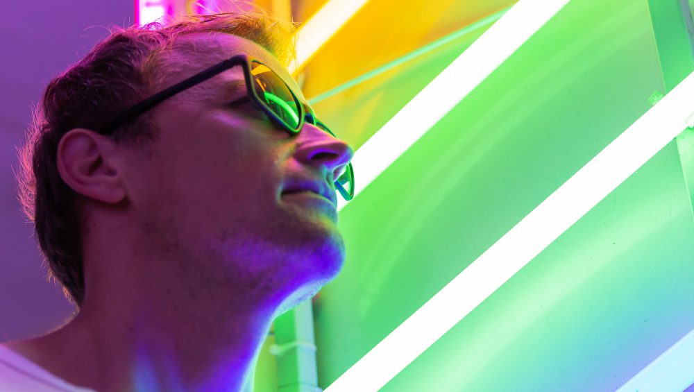 Man wearing sunglasses against multicoloured neon lights.
