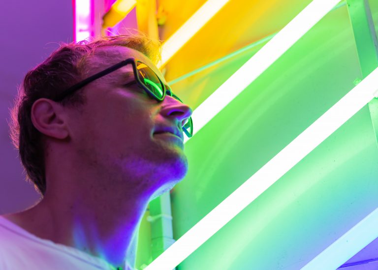 Man wearing sunglasses against multicoloured neon lights.