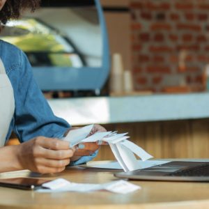 Shop owner checking receipts at table with laptop.