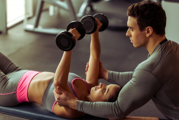 Sports coach assisting woman training with weights.