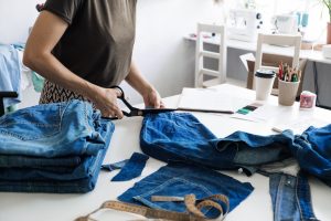 Person cutting up old denim jeans with dressmaking scissors.