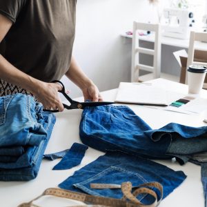 Person cutting up old denim jeans with dressmaking scissors.