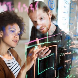 Two people discussing project ideas written on clear board.