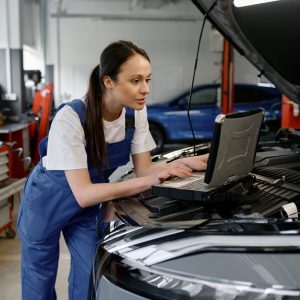 Female automotive engineer providing computer diagnostics using laptop.