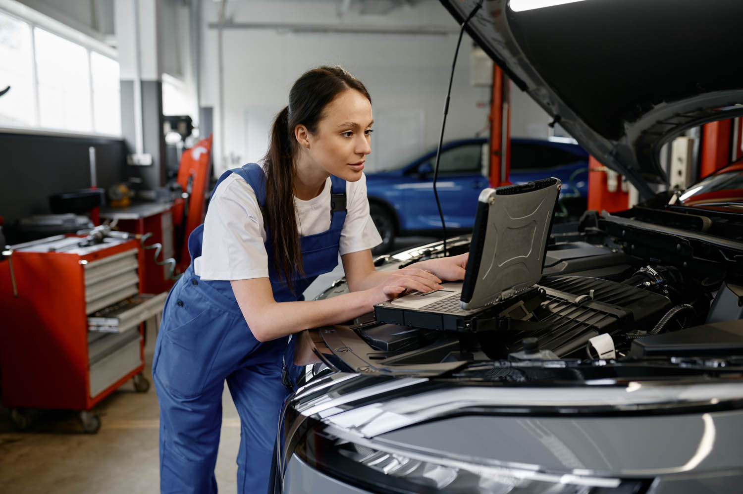 Female automotive engineer providing computer diagnostics using laptop.