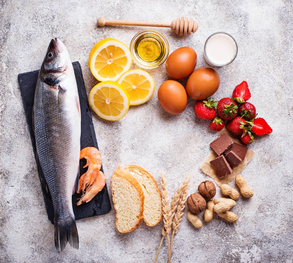Fish, prawns, lemons, honey, eggs, cream, strawberries, chocolate, nuts, wheat and bread on table