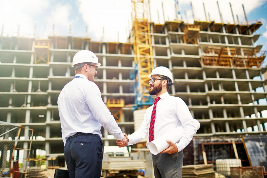 Engineers shaking hands outside building being constructed.