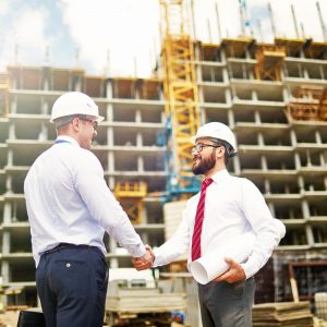 Engineers shaking hands outside building being constructed.