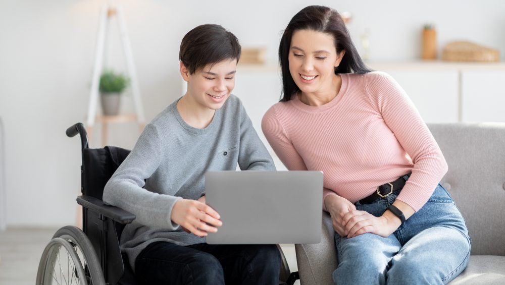Teen in wheelchair showing woman something on laptop.