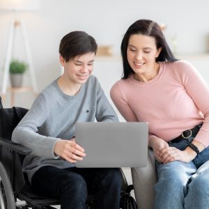 Teen in wheelchair showing woman something on laptop.