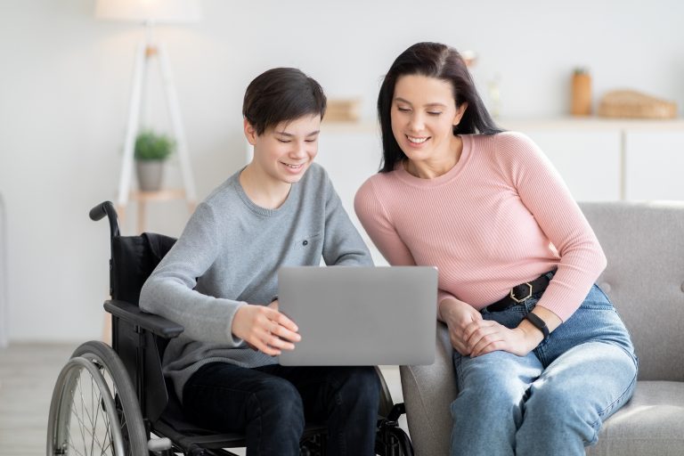 Teen in wheelchair showing woman something on laptop.