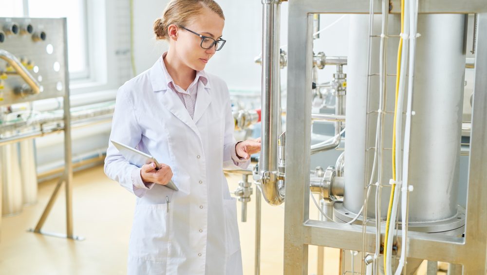 Woman wear lab coat inspecting food/liquid tank.