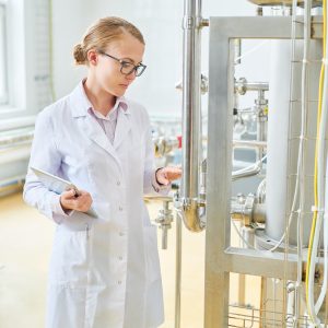 Woman wear lab coat inspecting food/liquid tank.