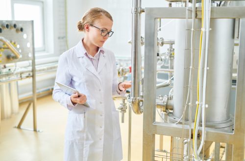 Woman wear lab coat inspecting food/liquid tank.