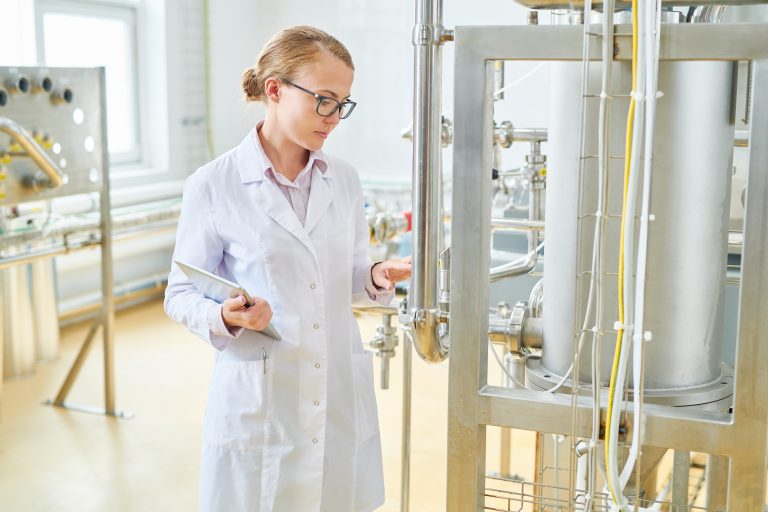 Woman wear lab coat inspecting food/liquid tank.