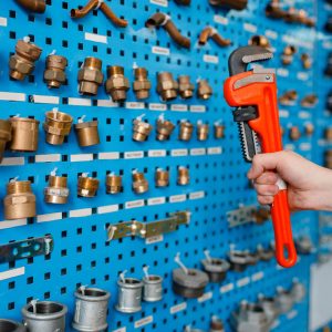 hand holding a wrench in front of rack of various brass bolts