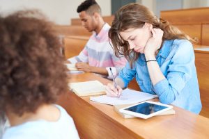 Person writing in notepad in lecture hall
