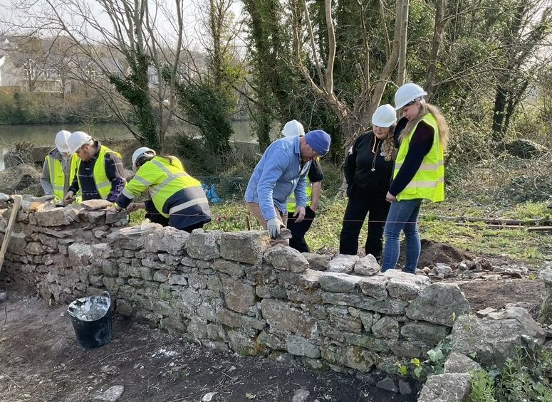 Group of learners and staff repairing old stone wall