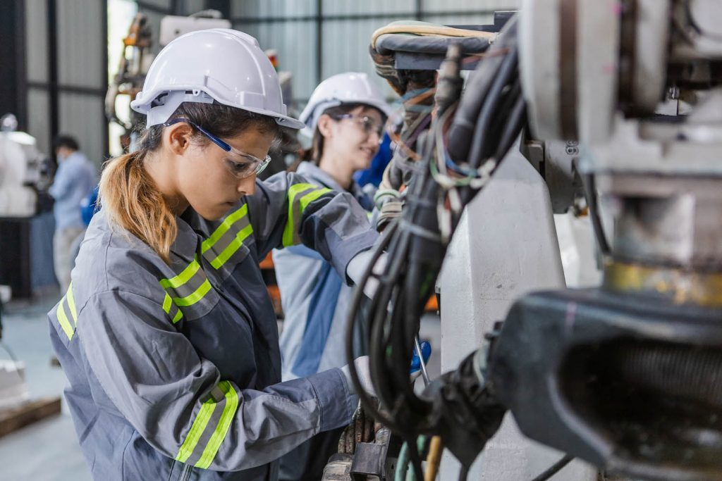 Two female engineers using tools to maintain robotic arm.