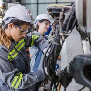 Two female engineers using tools to maintain robotic arm.