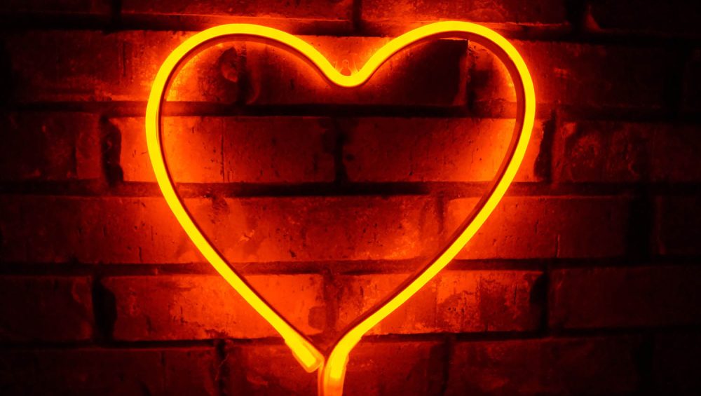 Orange neon light shaped as heart against a brick wall.