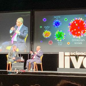 People sitting on stage discussing with big screens behind.