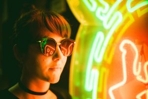 portrait of a person wear glasses next to neon sign