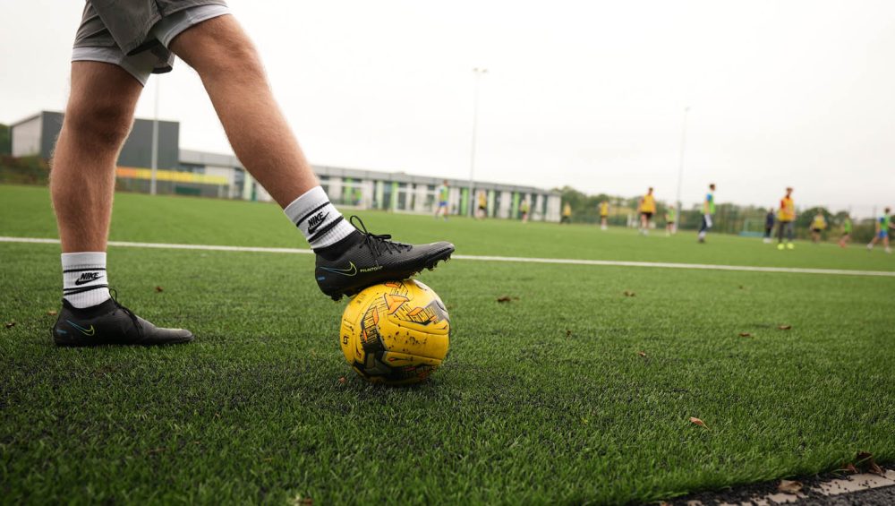Mans legs with foot resting on a football outside in field