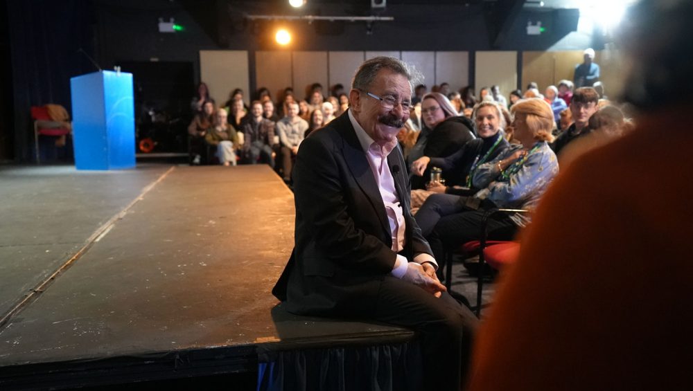 Professor Winston sat on Merlin Theatre stage smiling at audience during a Q&A