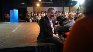 Professor Winston sat on Merlin Theatre stage smiling at audience during a Q&A