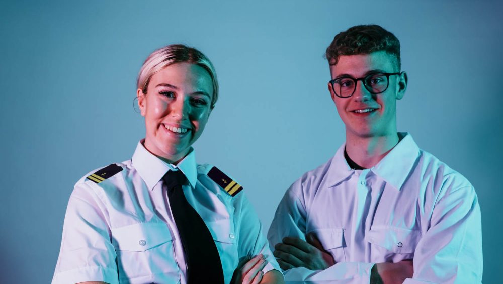 Two students against blue background wearing maritime uniforms.
