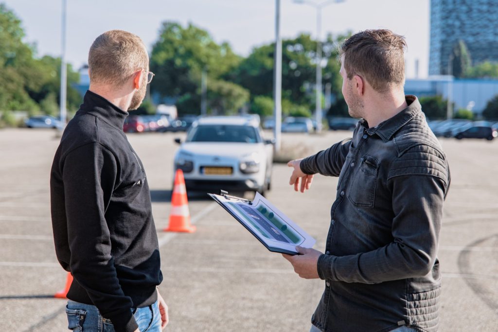 Two men standing with a clipboard pointing at car