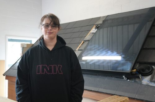 Learner Amy stands smiling in front of solar panels